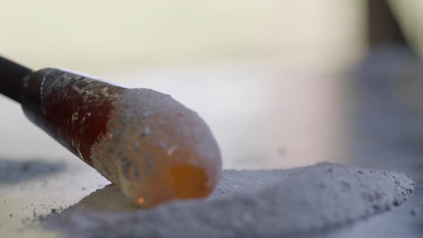 A glassblower rolls molten glass into a powder