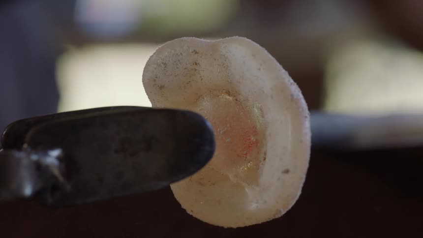 A glassblower stretches a clump of glass attached to the end of a rod