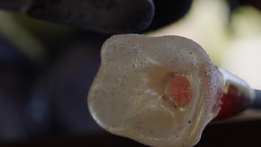 A poll with molten glass on the end being shaped by a tool