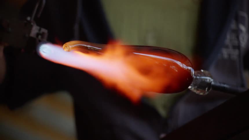 An artist uses a torch on a blown glass creation