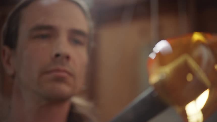 A man looks carefully at a piece of blown glass still on a pole