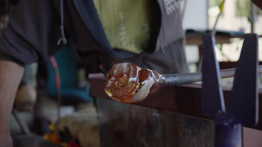 Man rolls molten glass into shape in glassblowing workshop