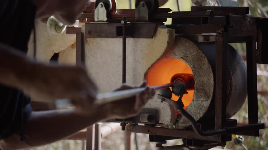 A glass blower turns a piece of glass in a kiln