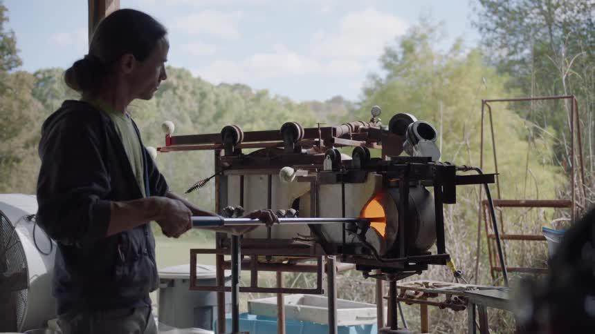 A glass blower heats up glass in a fire