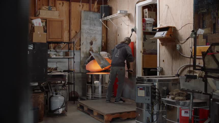 Man takes a ball of molten glass out of hot forge with a staff