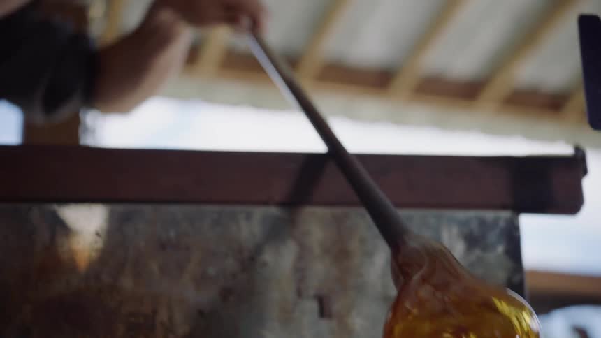 Man polishes and then works blown glass on metal tube