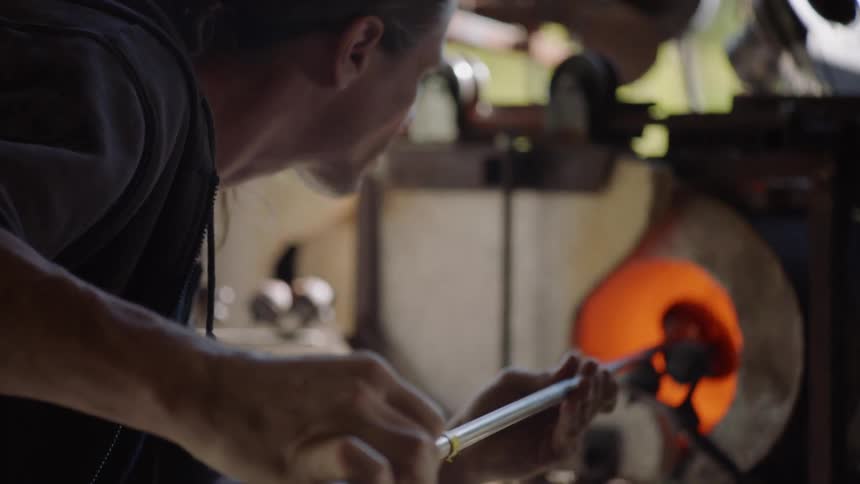 Glass maker turns glass in furnace on metal pole
