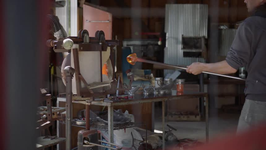 A man uses a long pole to take blown glass out of a kiln