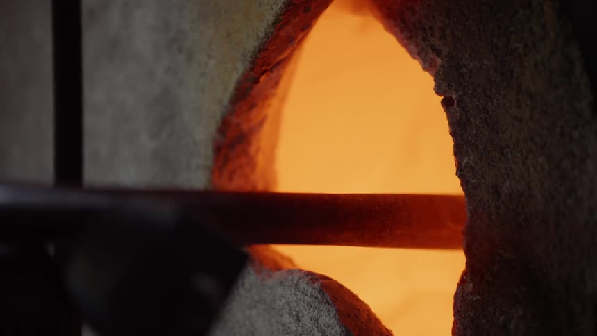 A glassblower pushes a stick of molten glass into a kiln