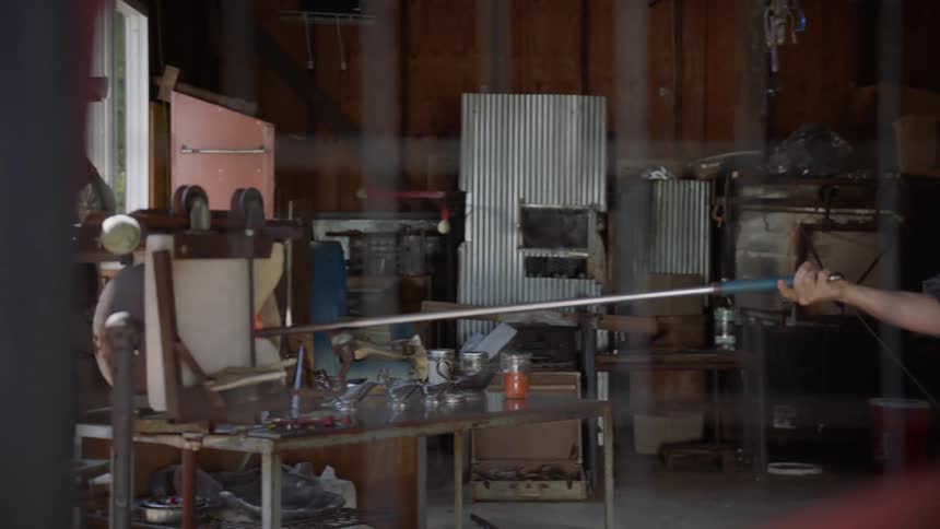 A man is holding a pole into an oven in his workshop