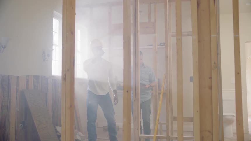 Two construction workers walk through an indoor construction site