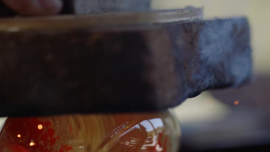 Man policies glass donut with hot pumice stone releasing sparks