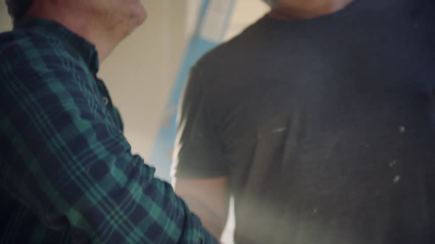 Two men shake hands while inside a home with a ladder