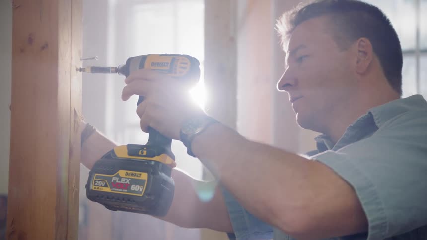 A man uses a drill to put a screw into wood
