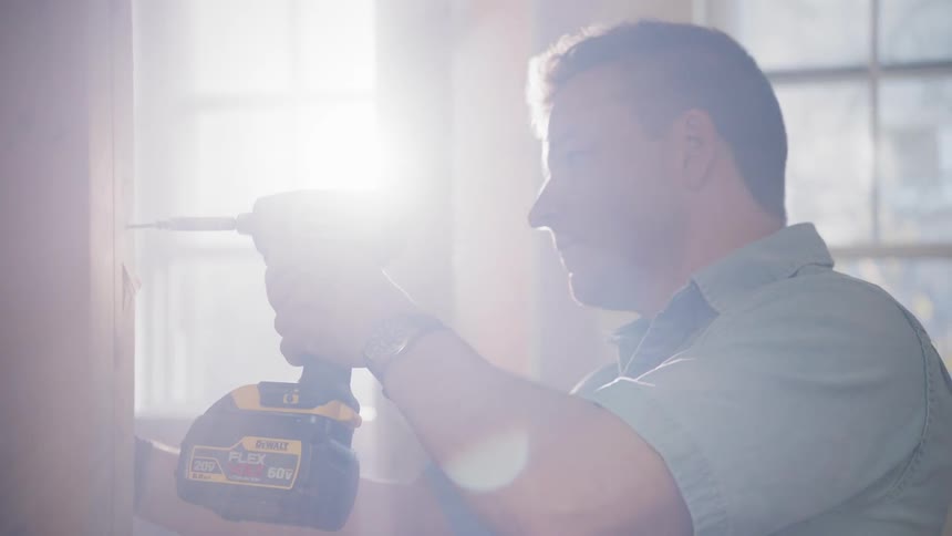 A man uses a power drill on a wood beam indoors