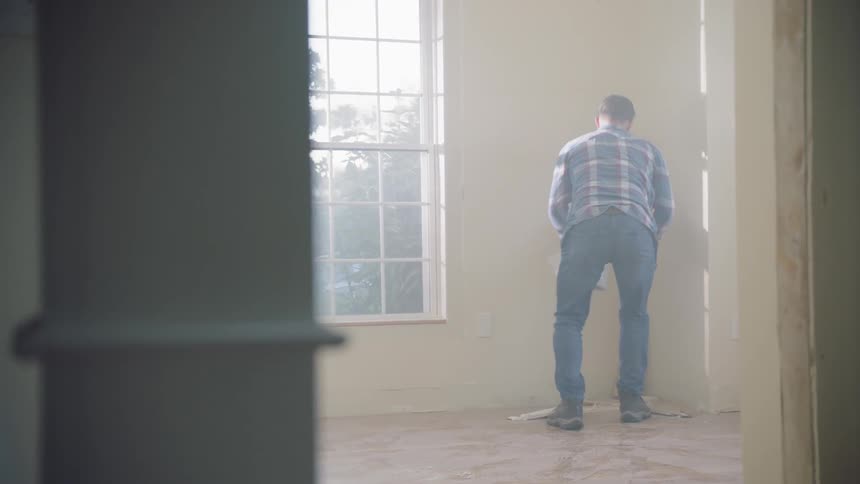 Male construction worker picks up scraps of wood sitting in the corner of the room and walks away