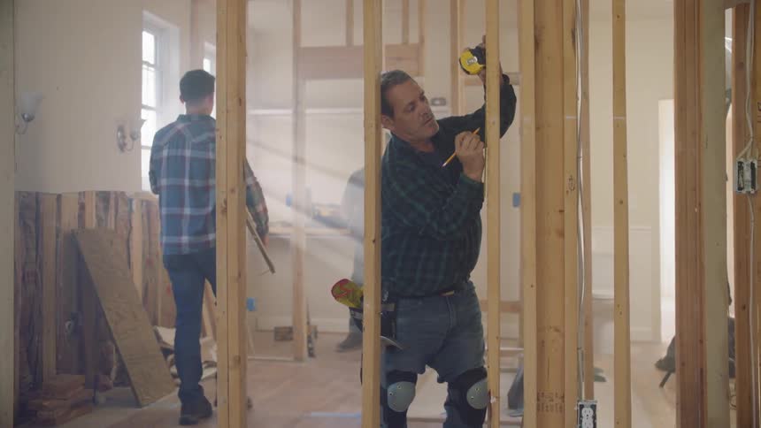 A carpenter marks locations on a wood support beam