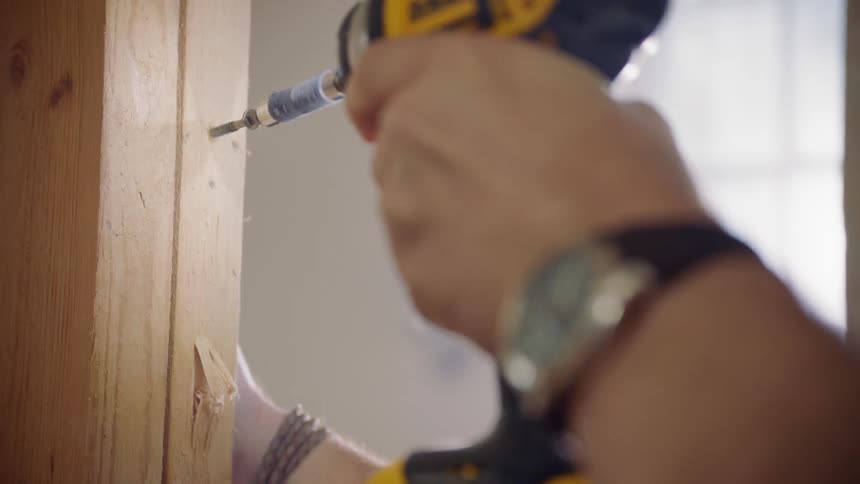 A construction worker uses a drill to drive a screw into wood