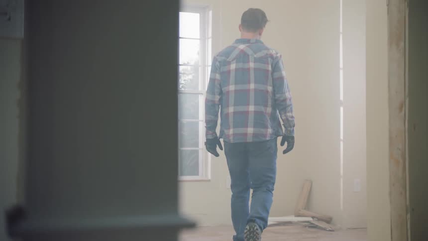 A carpenter picks up scraps of wood in an empty room