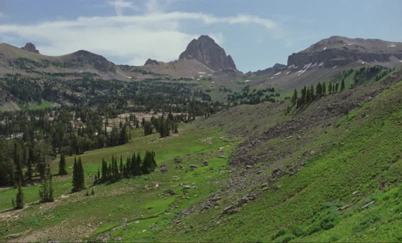 Green hills trees and rocky peaks on a blue sky day