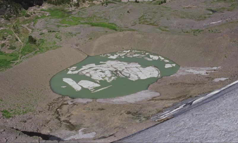 Ice floats on green lake in middle of bare ground near mountains