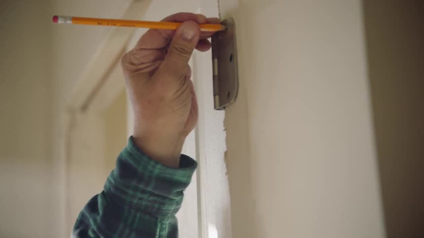 A man marks where a door hinge should be hung on a wall