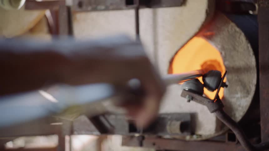 A man turns a long rod as he heats glass in a furnace