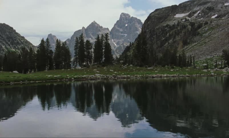 Trees and rocky hills are reflected on the rippling surface of a lake