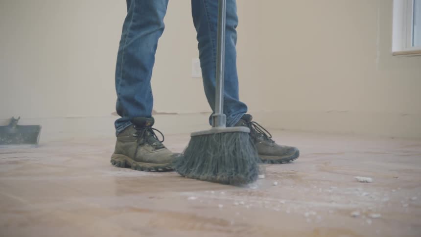 Person uses broom to sweep in empty tiled room near window
