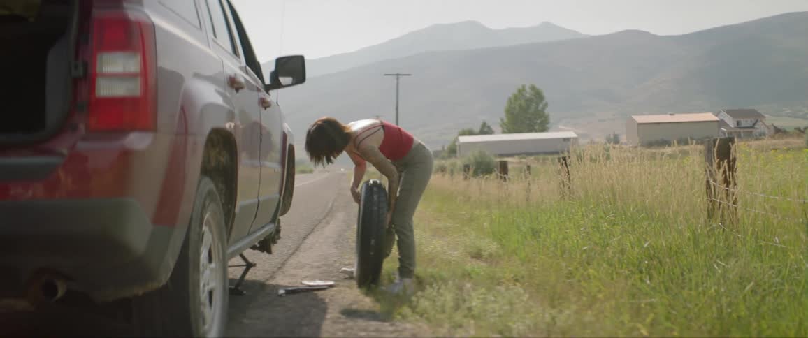 Young woman changing a car tire on side of the road in the country