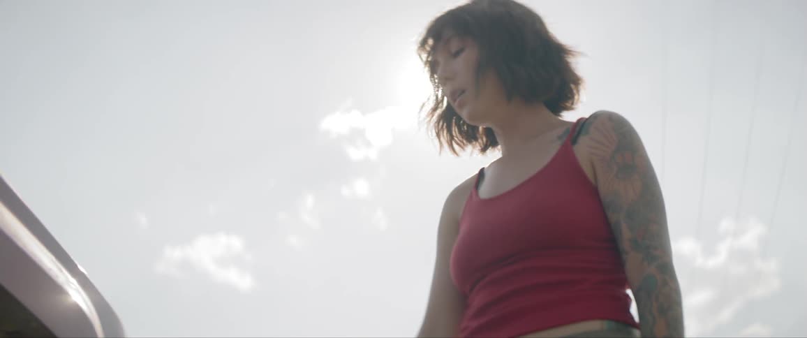 A woman uses her arm to wipe sweat off her face and push her hair back on a hot sunny day