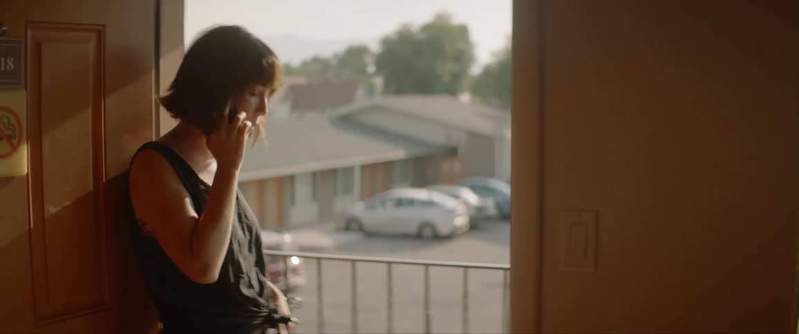 Woman talks on phone while leaning against open door at motel