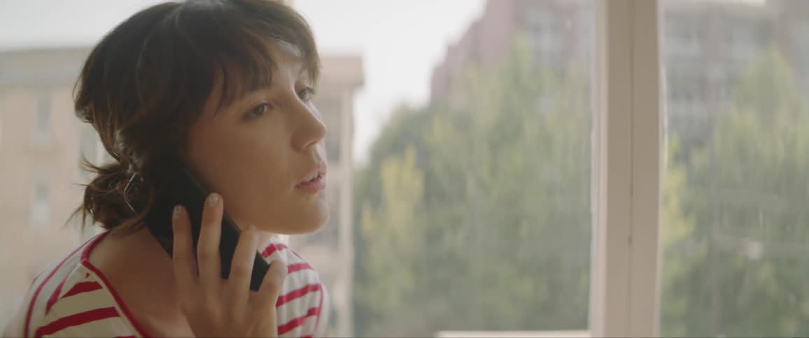 A young woman sits beside a window talking on a cell phone