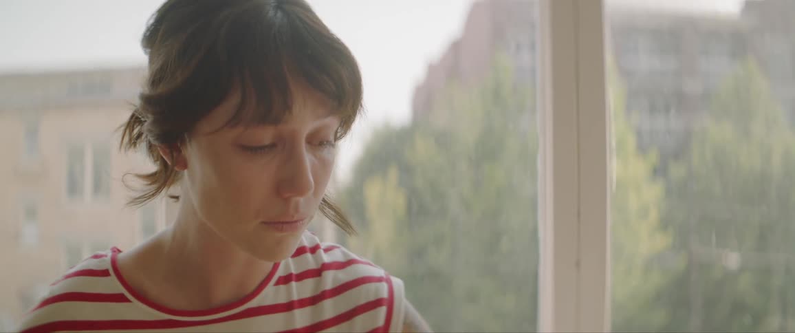 A woman wipes her eyes by the window