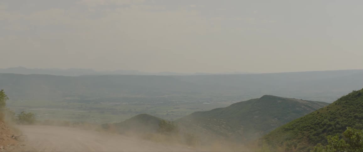 A red suv drives along a dirt road through the hills leaving a trail of dust behind