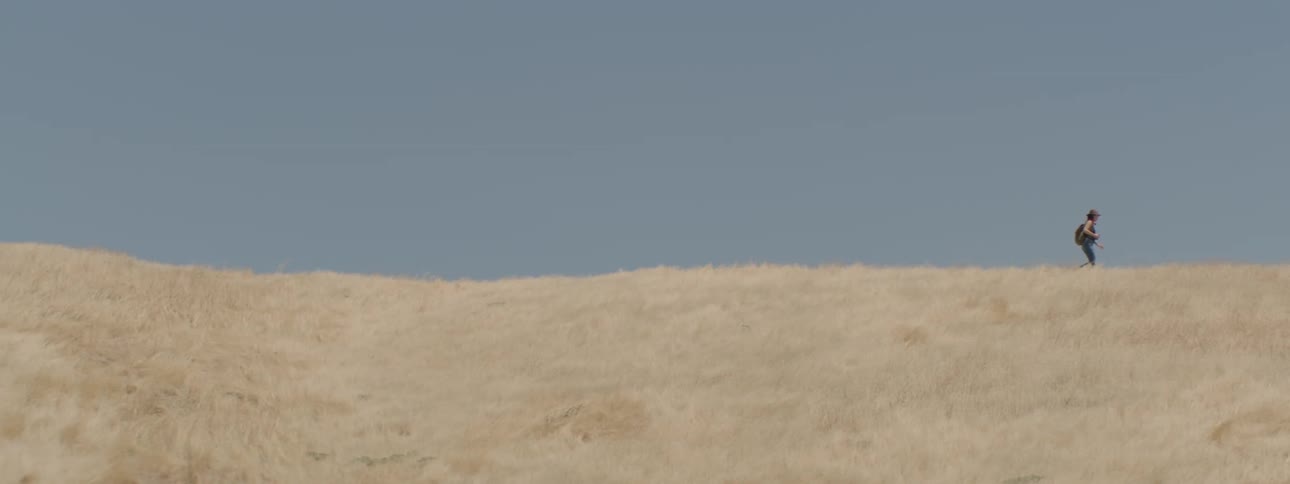 A woman walks across a grassy hill