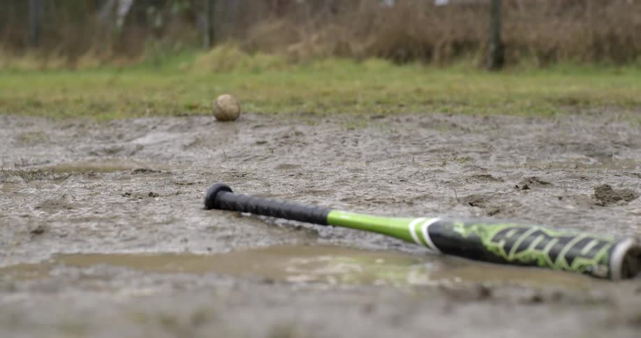A boy hits a baseball and runs to first base on a muddy field