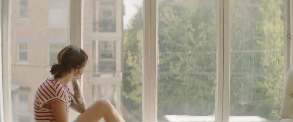 A woman walks over to the window to sit and use the phone