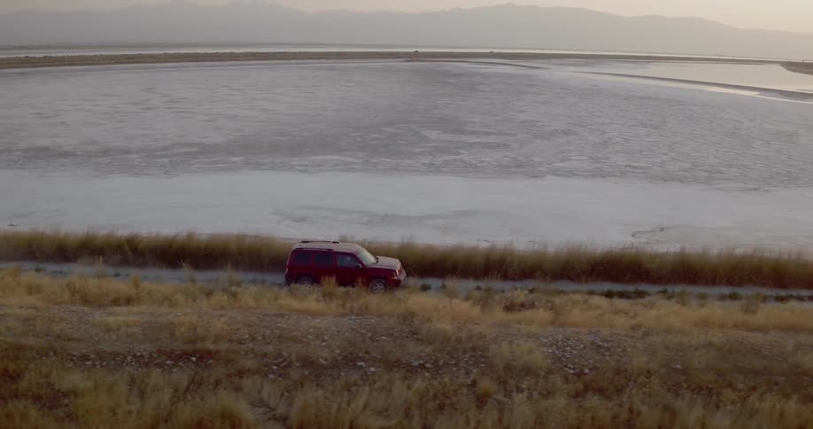An suv travels a road beside a lake and dead grass