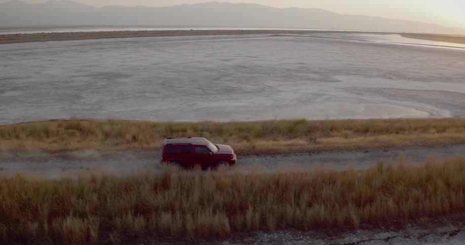 Aerial view of a red suv driving on a dirt road alongside a flooded field