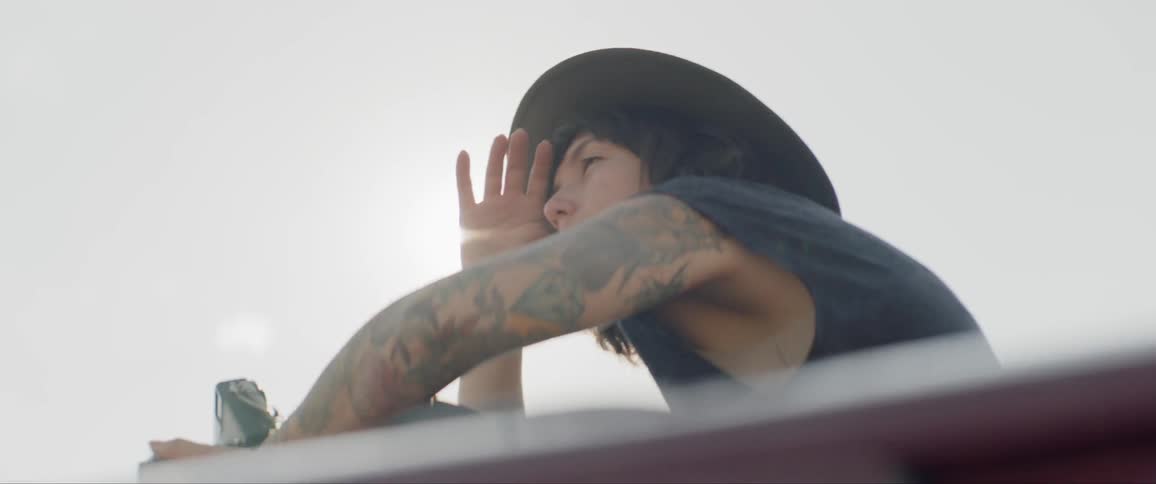 A woman stands out of a car sunroof and holds a camera