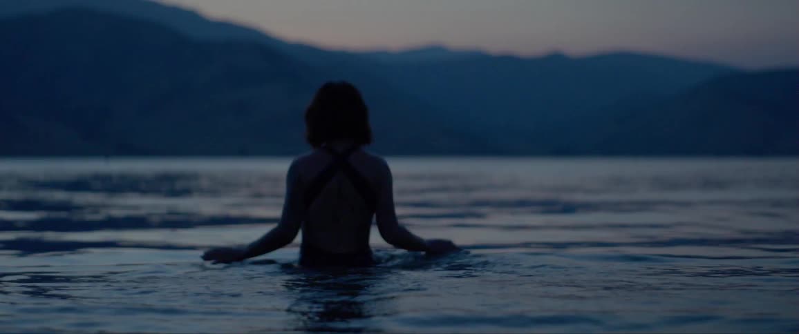Woman wearing swimsuit enters a lake surrounded by mountains at dusk