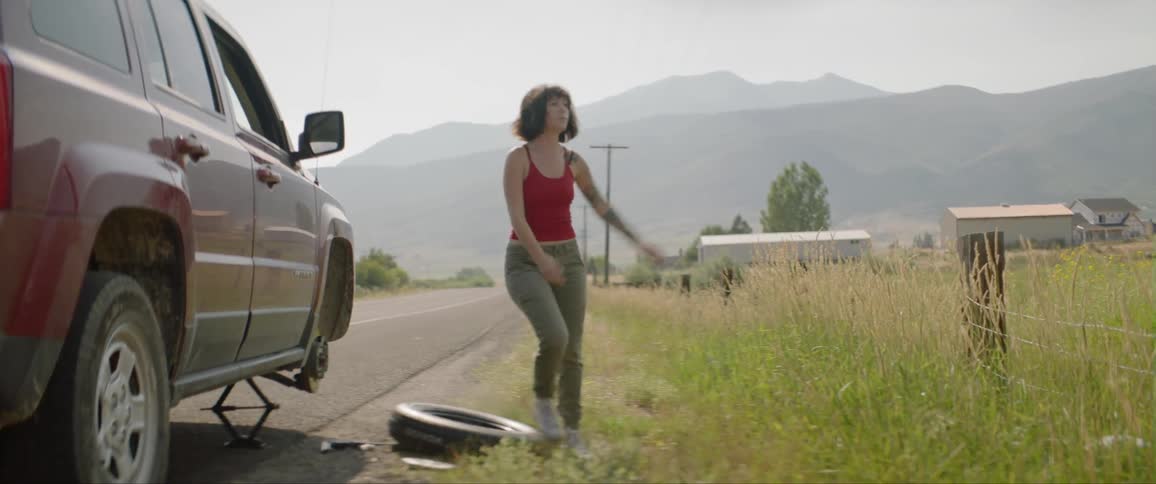 A young girl kicks at her tire at the side of the road