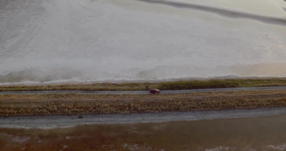 A vehicle drives on a road beside a frozen lake