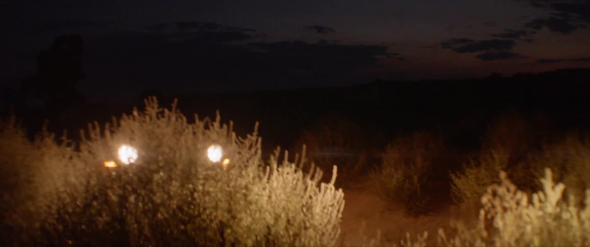 Car with headlights on driving on a country dirt road at night