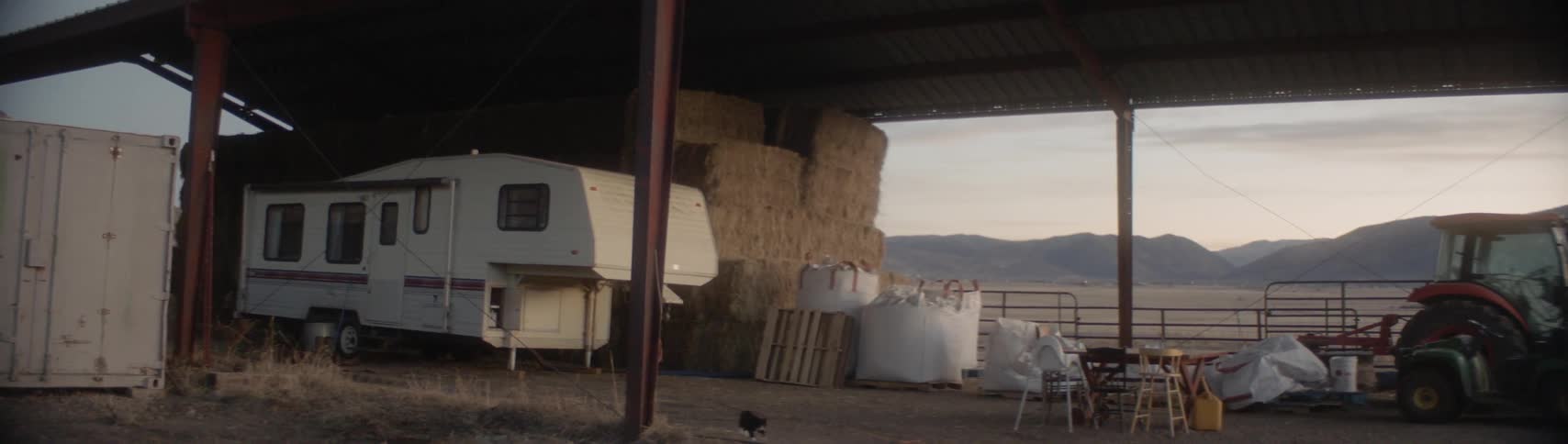 A camper hay bales and farm equipment are stacked under an outdoor awning