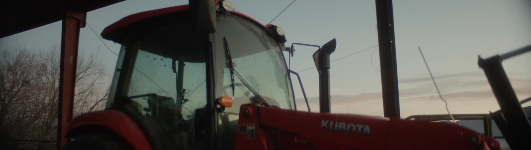 A tractor is parked on a farm at sunrise