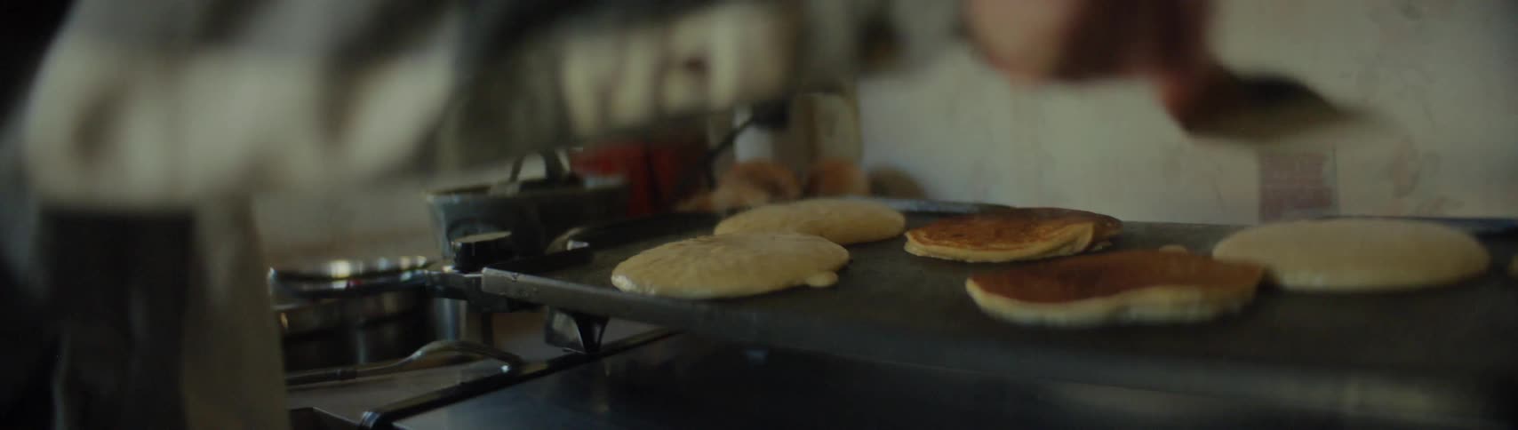 A man flips pancakes cooking on a griddle in a home kitchen