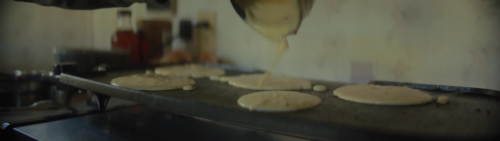 A white person pours pancake batter on a grill