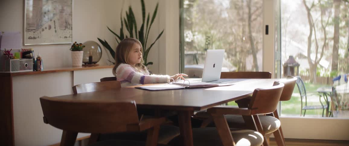 A girl using a laptop at a table in a house during the day